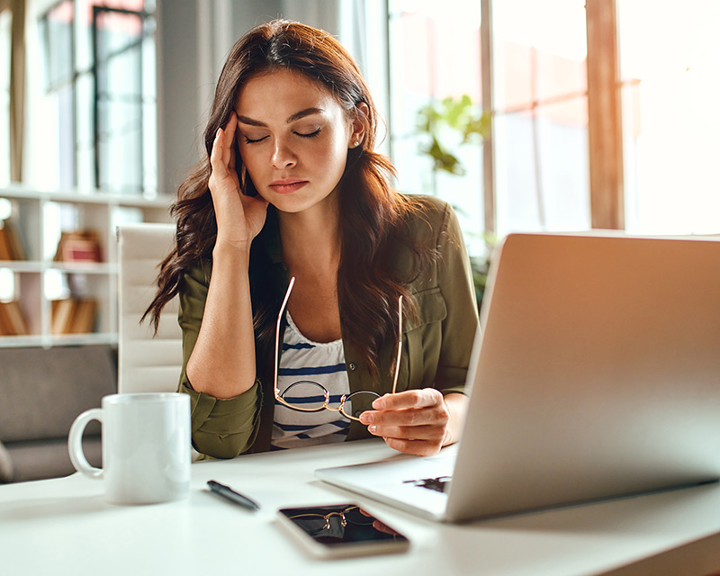 Tired woman sitting at a laptop with a cup of coffee. Needs to vent with a therapist who specializes in women's issues.